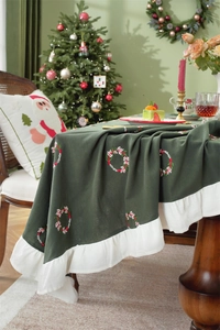 Detailed embroidery of Christmas wreath on green cotton tablecloth with white ruffled edges