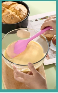 Pink silicone spatula mixing cake batter in glass bowl during professional baking
