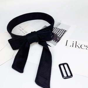 Detail of a large black velvet bow belt with an adjustable buckle on a minimal background