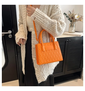 Détail d'un sac à main matelassé orange porté avec un cardigan en maille blanche