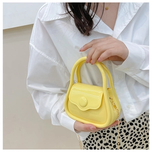 Close-up of vibrant yellow mini jelly bag with gold chain strap held by model