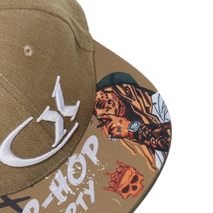Detail of khaki hip-hop cap featuring white embroidery and graffiti art on the flat brim