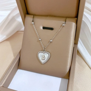 Macro view of heart-shaped shell pendant with V-letter detail in a beige jewelry box