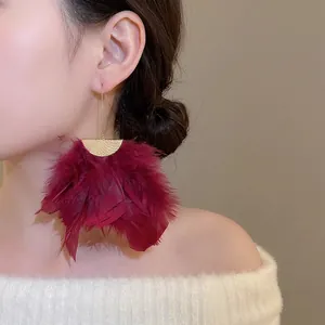 Burgundy feather tassel earrings with gold crescent studs worn by a female model