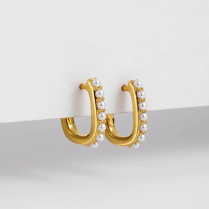 Detailed view of U-shaped gold earrings with embedded pearls on a white surface
