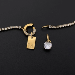 Dettaglio di collana in acciaio al titanio placcato oro 14K con strass e ciondolo M