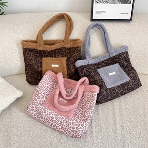 Close-up of leopard print plush tote bags in brown, grey, and pink on a soft sofa