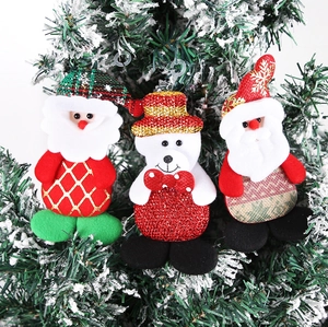 Detail of plush Santa and bear ornaments hanging on a snowy Christmas tree branch