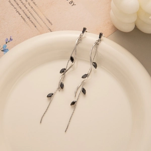 Macro shot of silver leaf tassel earrings with black stones on a white ceramic plate
