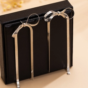 Detail of silver bow tassel earrings with snake chain texture on a jewelry box