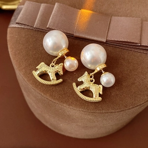 Detail of rocking horse and pearl drop earrings on a brown velvet jewelry box