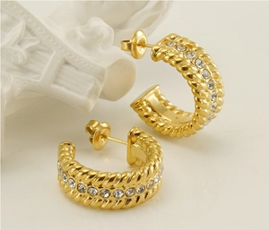 Detailed view of U-shaped gold earrings with twisted rope texture and pavé crystals