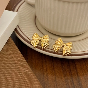 Detailed view of vintage gold bow earrings with radial texture on a ceramic cup edge