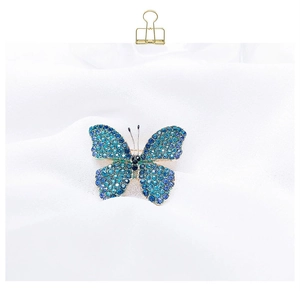 Detail of blue gradient crystal butterfly brooch with gold alloy base on white fabric
