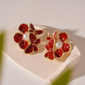 Detail of red enamel flower earring with central pearl on a minimalist stone surface