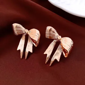 Rose gold bow stud earrings with vertical pleated texture on dark red silk background
