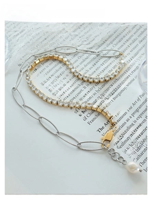 Macro detail of layered paperclip chain and tennis chain with zircon and pearl charm