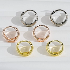Three pairs of C-shaped hoop earrings in silver, gold, and rose gold on white steps