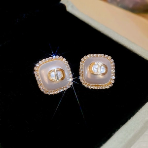 Macro shot of gold-plated square stud earrings featuring crystal halo and CD logo