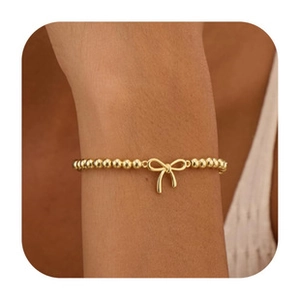 Detail shot of a golden beaded bracelet featuring a delicate bow charm on a model's wrist