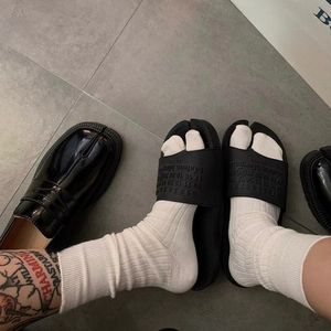 Detail of white split-toe socks worn with black tabi slides and classic loafers
