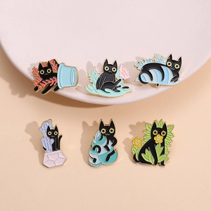 Set of six cute black cat enamel pins featuring plants and cacti on a soft pink ceramic plate