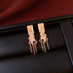 Macro shot of 18K rose gold plated earrings with leaf pattern and tassels on black leather
