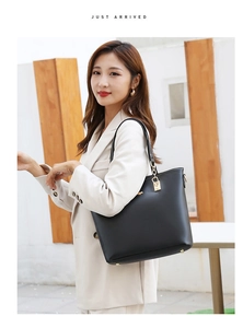 Chic black tote bag with gold buckle hardware and thin strap held by a stylish model