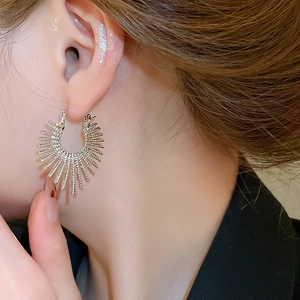 Close-up of a model wearing golden sunburst hoop earrings with a textured C-shape design