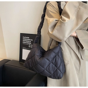 Close-up of a black quilted puffer bag worn by a model in a minimalist setting