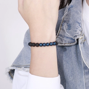 Close-up of 8mm black lava and blue matte agate beads bracelet on a denim sleeve wrist