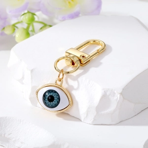 Detail of golden evil eye keychain with blue iris on white stone background