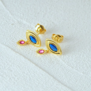 Macro view of gold stud earrings featuring marquise-cut blue and pink gems on sand texture