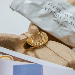 Polished gold horseshoe ring with clear zircon inlay on a textured aesthetic background