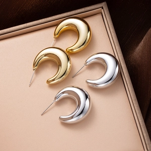 Polished gold and silver croissant stud earrings displayed on elegant brown satin fabric