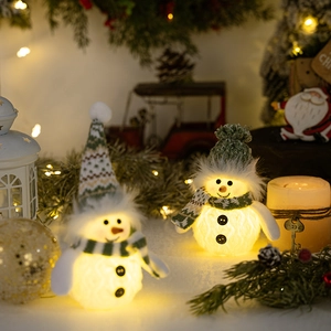 Close-up of glowing snowman dolls with green knit hats and warm LED lights inside