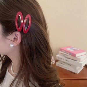 Detail view of red oval acetate hair clip with gold lettering on a female model side profile