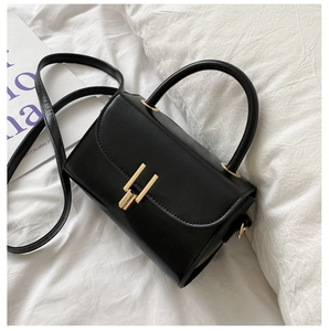 Detail of black faux leather handbag with golden metal clasp and slim shoulder strap