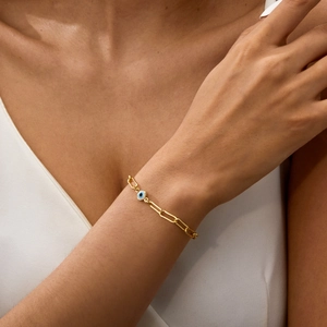Detail of paperclip chain bracelet with a blue evil eye charm worn on a female wrist
