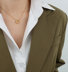 Close-up of a minimalist 18K gold-plated oval pendant necklace worn with a green blazer
