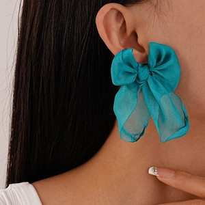 Detailed close-up of a large teal organza ribbon bow earring worn by a model