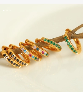 Détail de boucles d'oreilles créoles dorées avec zircons colorés sur une branche en bois