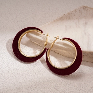 Detail of burgundy velvet and gold-plated geometric hoop earrings on a stone base