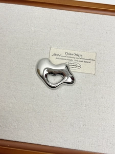 Macro view of silver liquid heart brooch on linen surface with mirror polish finish