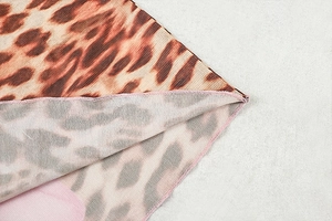 Dettaglio ravvicinato del tessuto leopardato con cuciture overlock rosa e trama a maglia