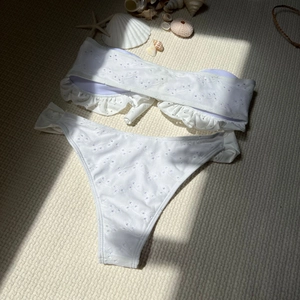 Close-up of white two-piece bikini with eyelet embroidery and ruffle detail on woven mat