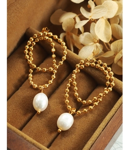 Close-up of double-loop gold bead earrings with teardrop pearls on brown velvet