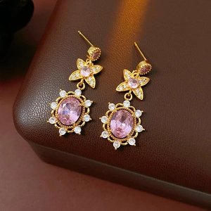 Detail of vintage gold earrings with pink gemstones and zircon on a leather surface