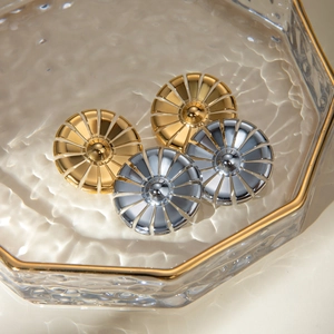 Goldene und silberne Gänseblümchen-Ohrringe aus Edelstahl auf einer Glasschale