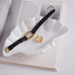 Vintage watch with black leather strap and gold ring in a white shell dish